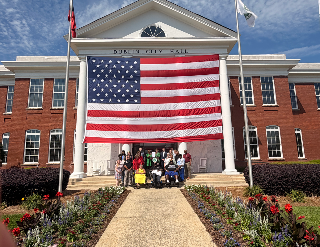 A group of people outside, standing under a extremely large American flag